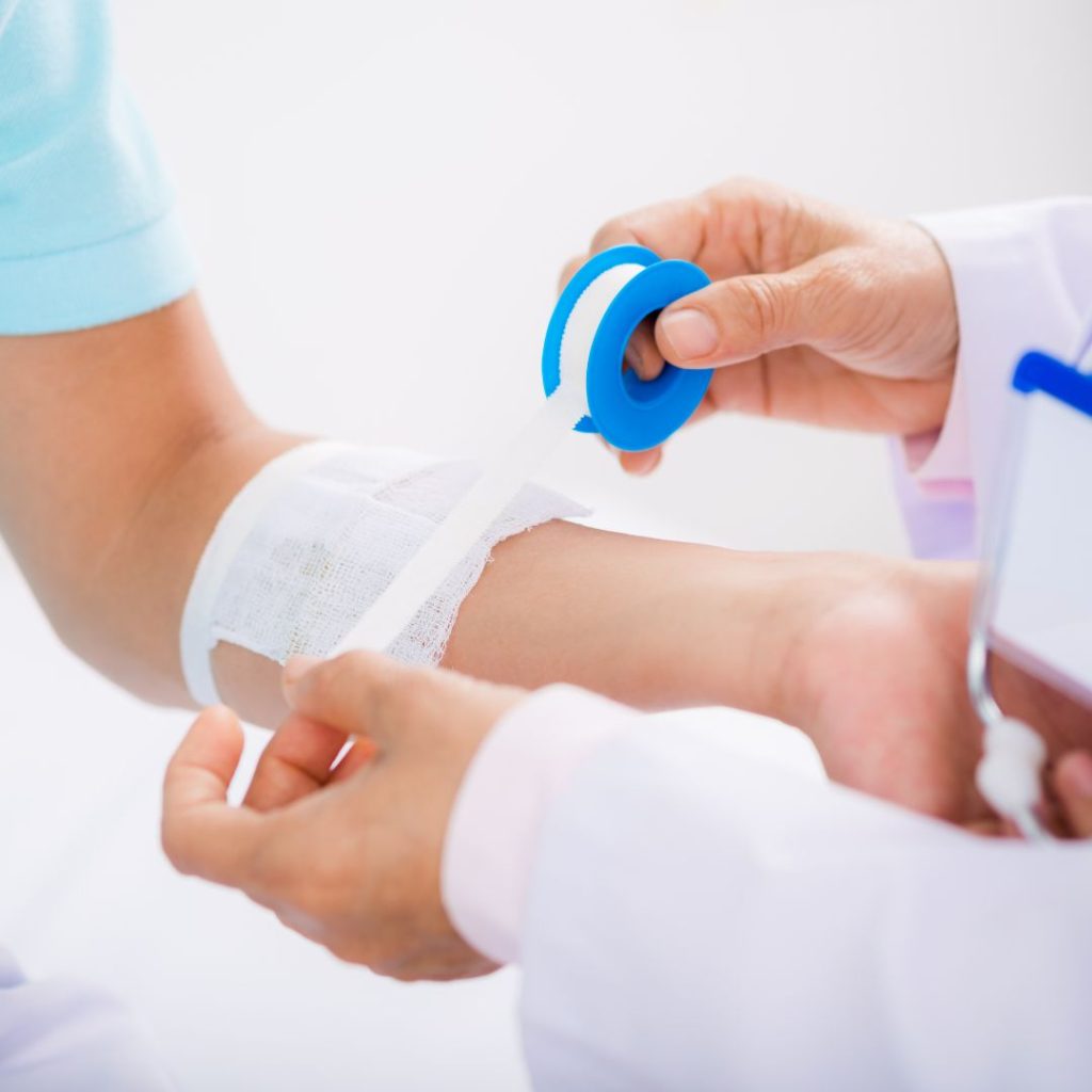 person puts gauze on patient arm using medical tape