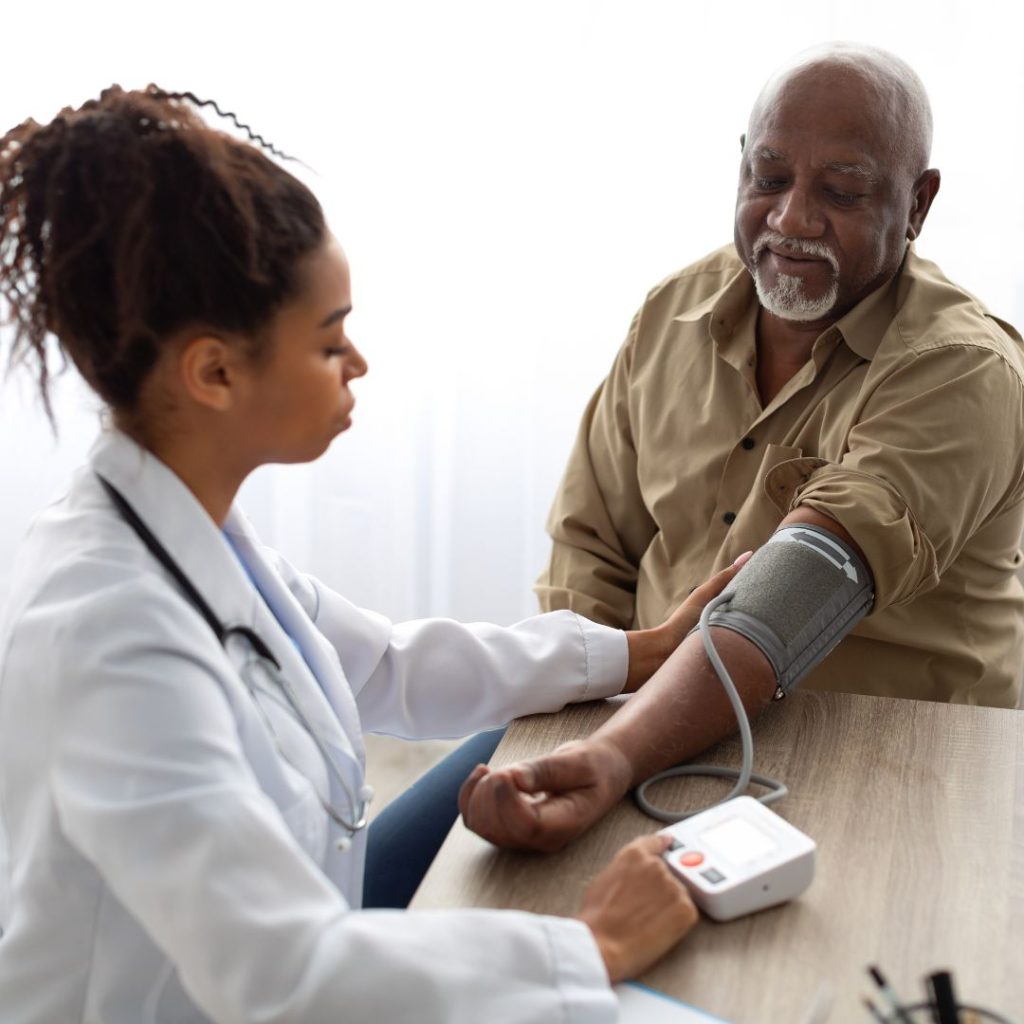 female doctor checks the blood pressure of man seated opposite her